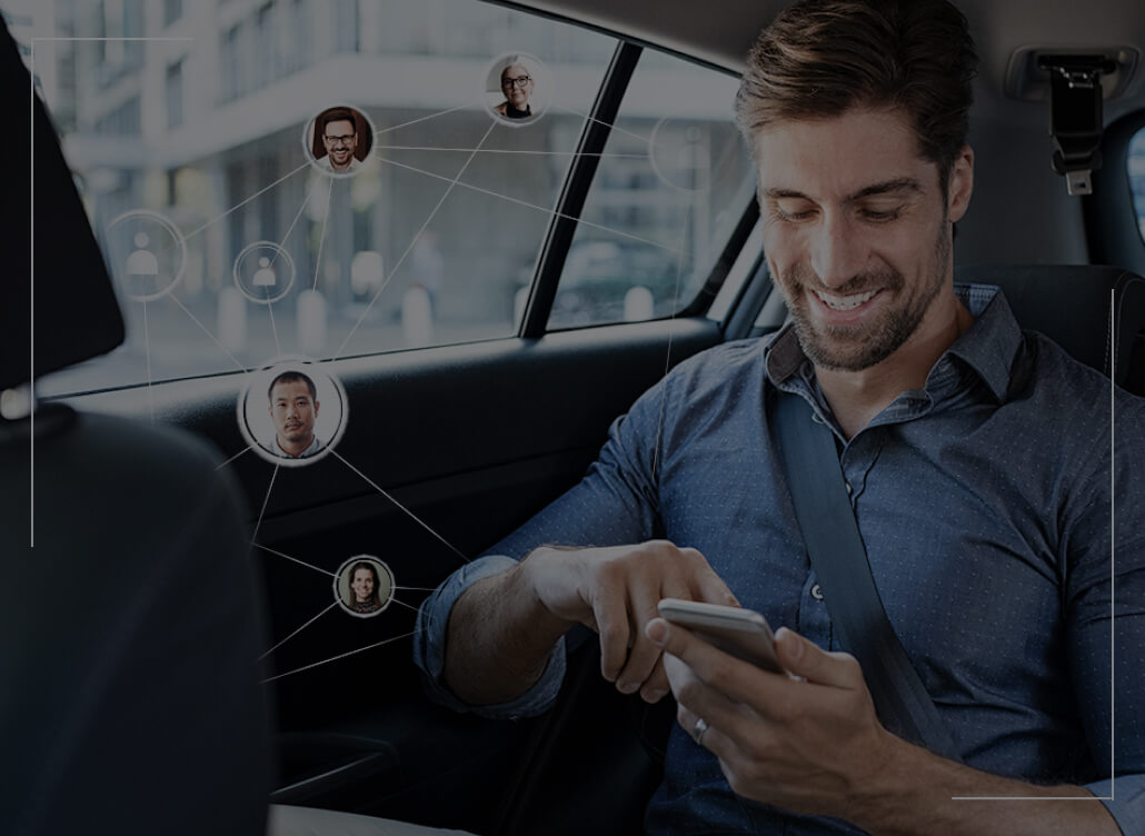 A man, as a passenger in a car, sits and looks at his phone.