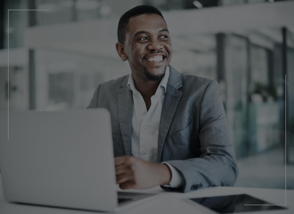 A man in a suit smiles as he sits in front of a laptop.